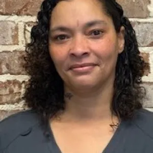 smiling woman with a grey merry maids uniform standing in front of a brick wall